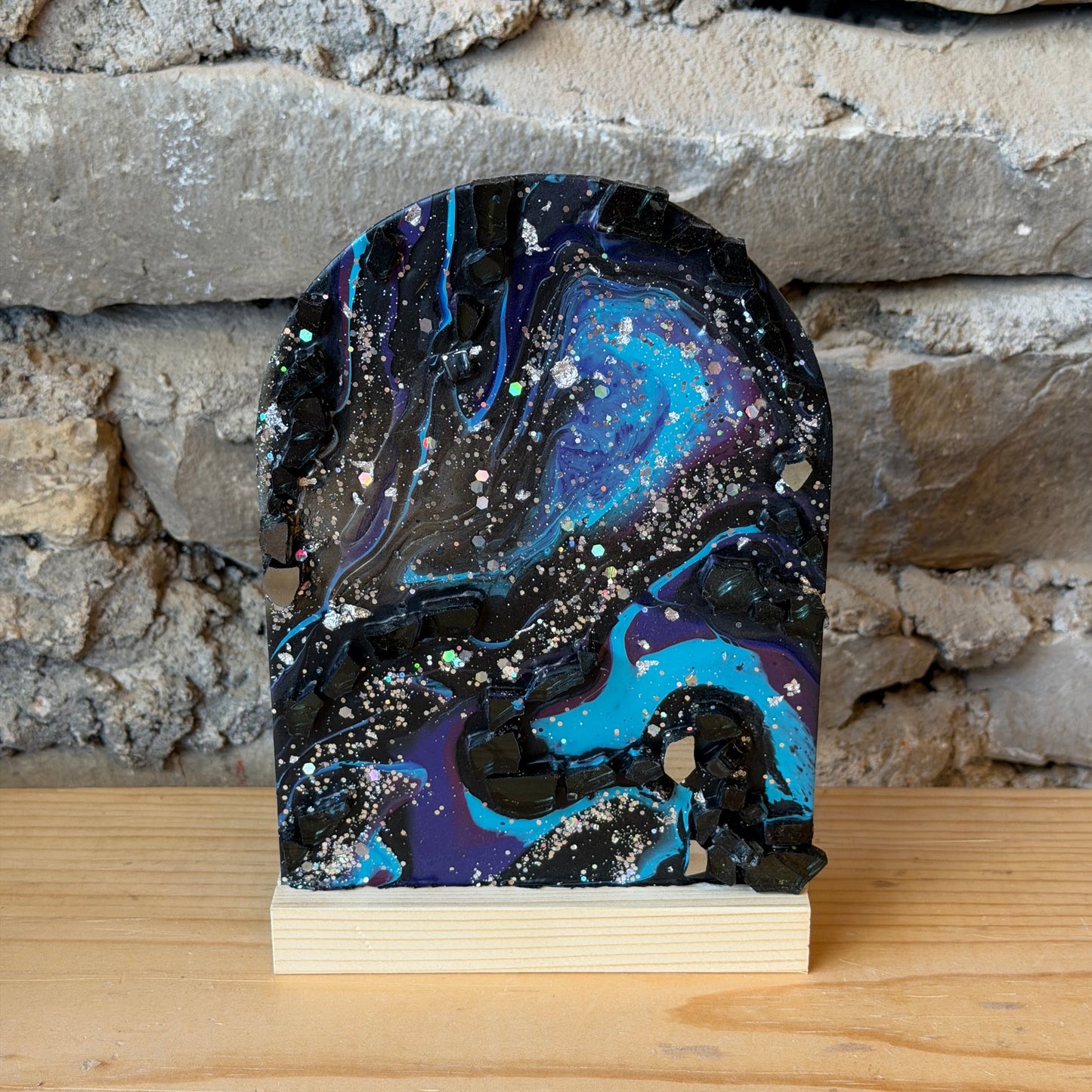 Decorative epoxy galaxy display with a blue and purple sky design attached to a wooden board against a stone wall.