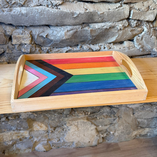Colorful wooden tray with a rainbow pride flag design on a stone wall background