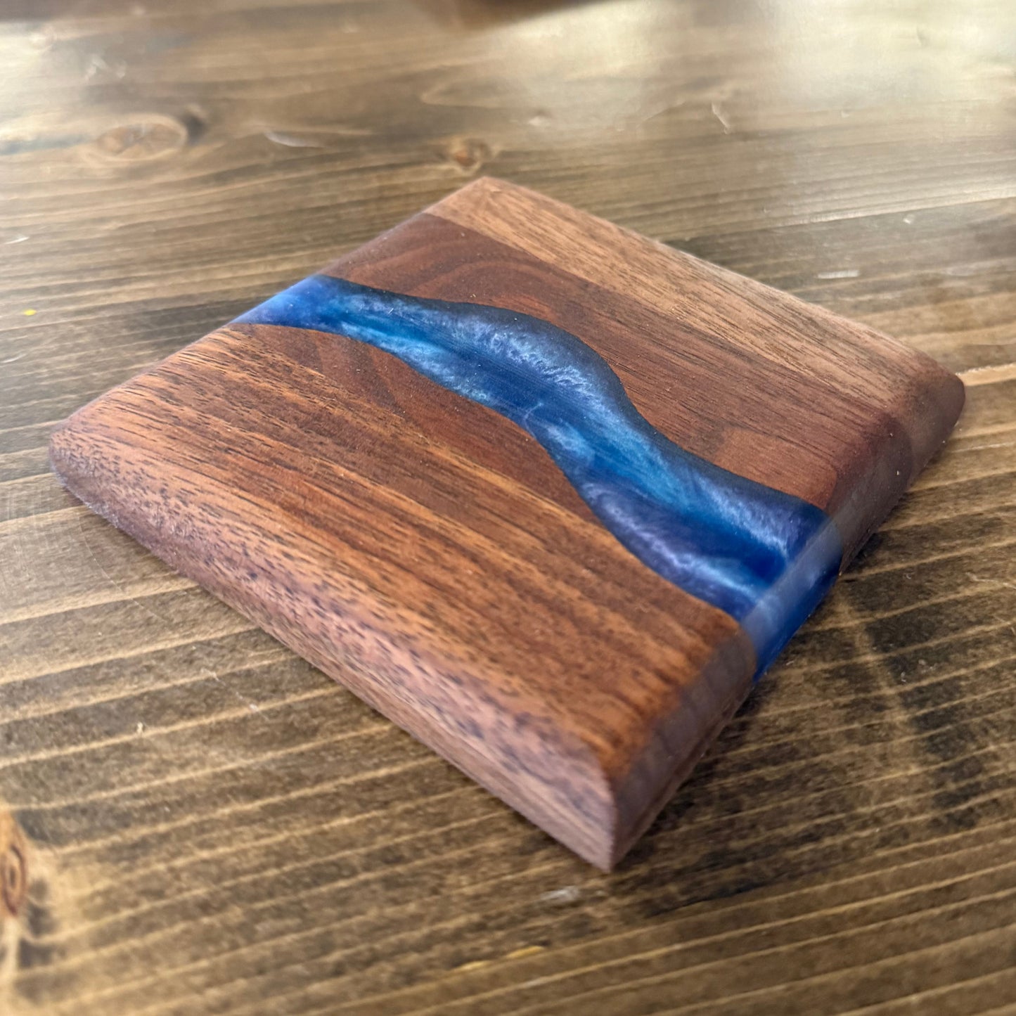 One wooden epoxy river coaster with blue resin inlay on a wooden surface