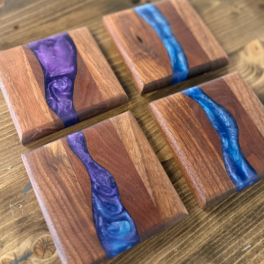 Four wooden epoxy river coasters with blue and purple resin inlay on a wooden surface