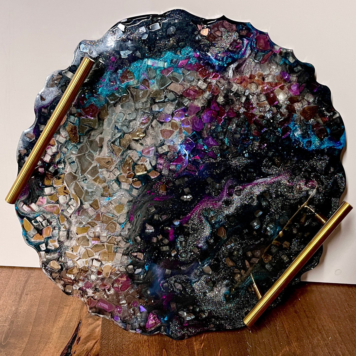 An epoxy tray with a multicolor epoxy geode design with a crystals and gold handles.