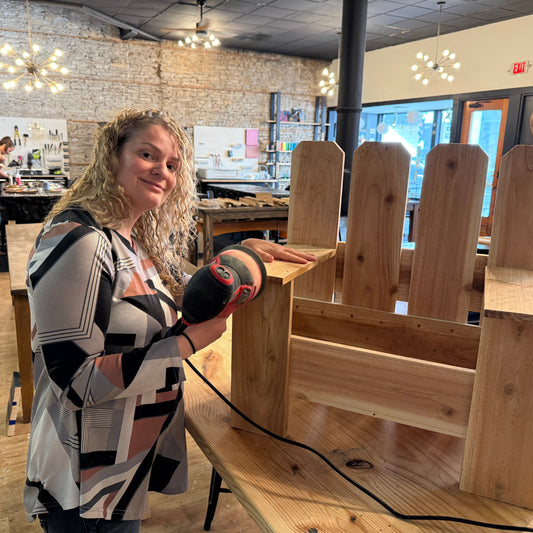 Woman using a sander on a wooden planter chair in a workshop setting