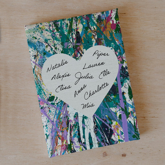 A canvas with a heart stencil in the center, surrounded by splatters of multicolored paint. The canvas has signatures of multiple participants.