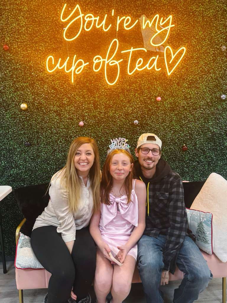 Family sitting together with a neon sign reading 'You're my cup of tea' in the background.