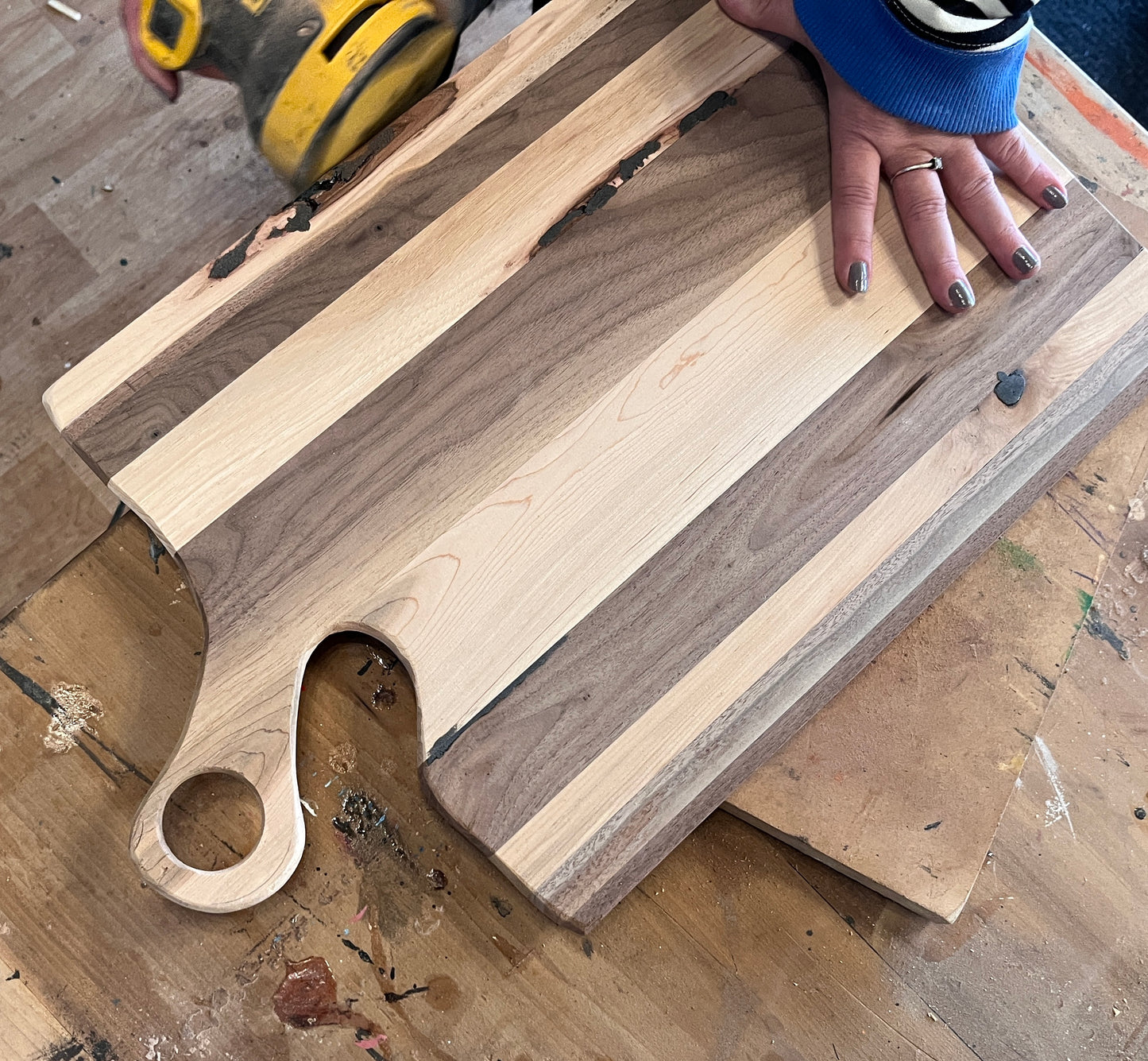 Wooden charcuterie board with a hand holding a power sander tool on a wooden surface