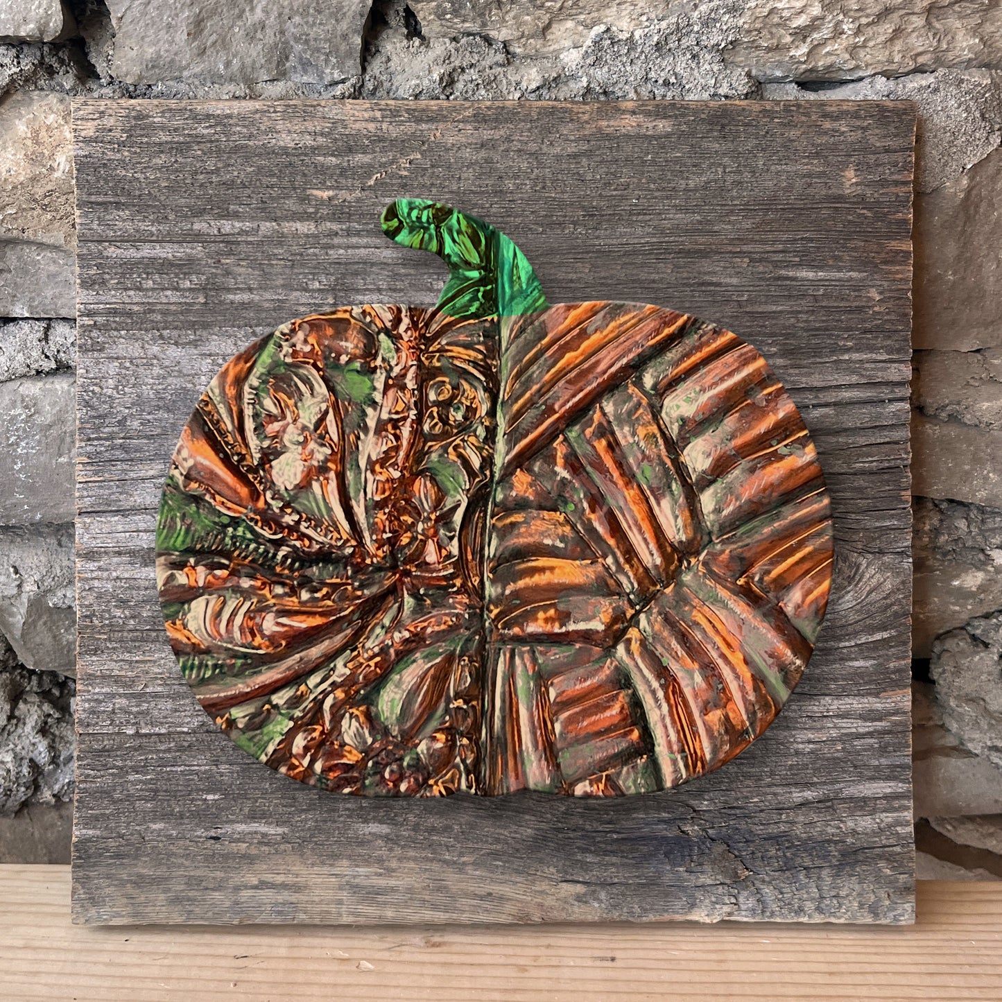 Decorative copper pumpkin on a wooden board against a stone wall.