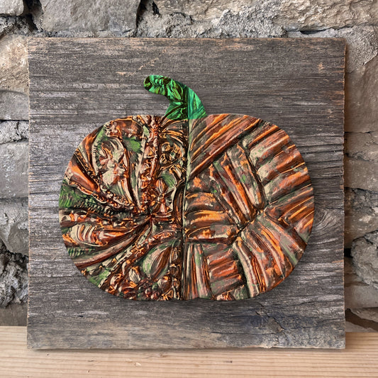 Decorative copper pumpkin on a wooden board against a stone wall.