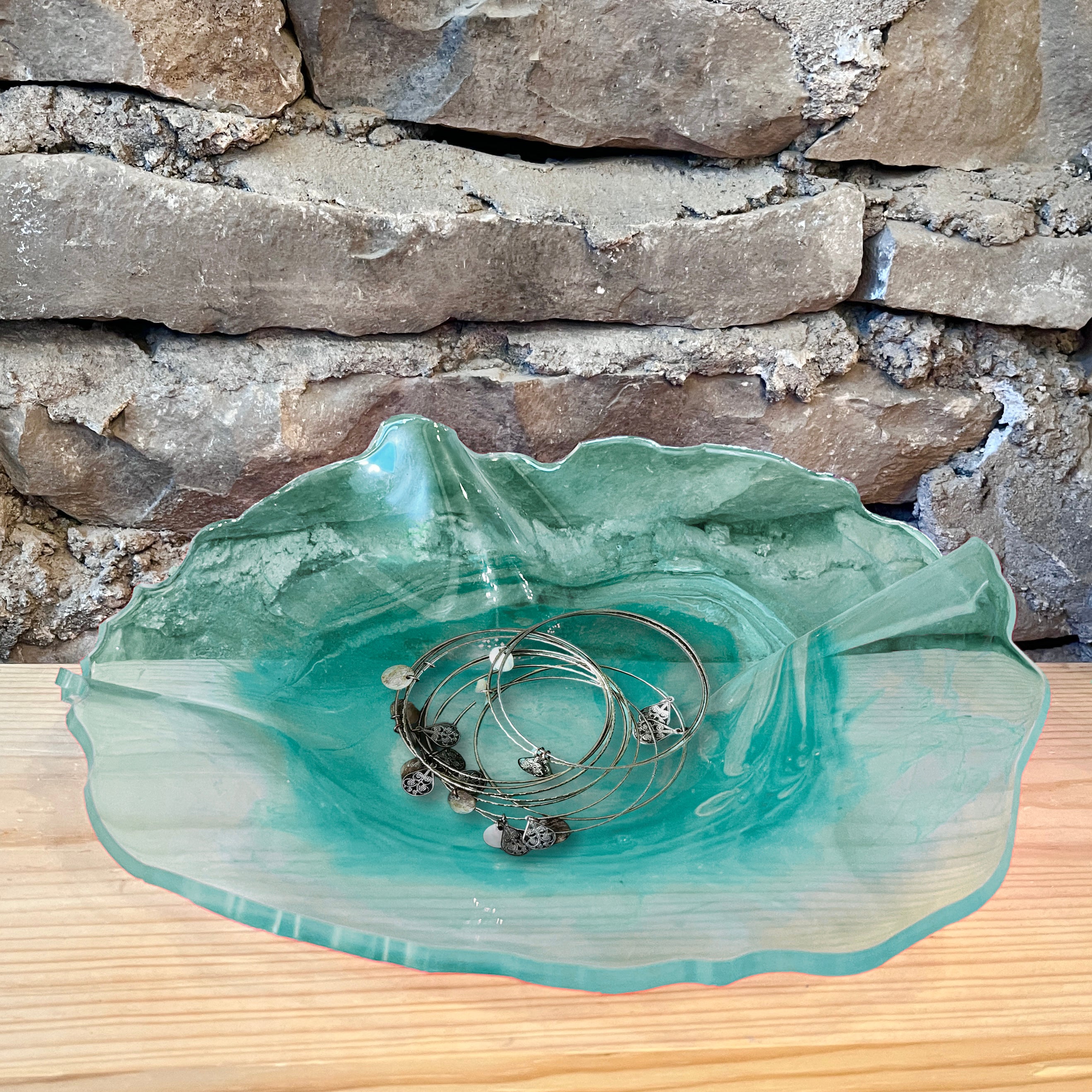 Turquoise epoxy dish with jewelry on a wooden surface and stone wall background