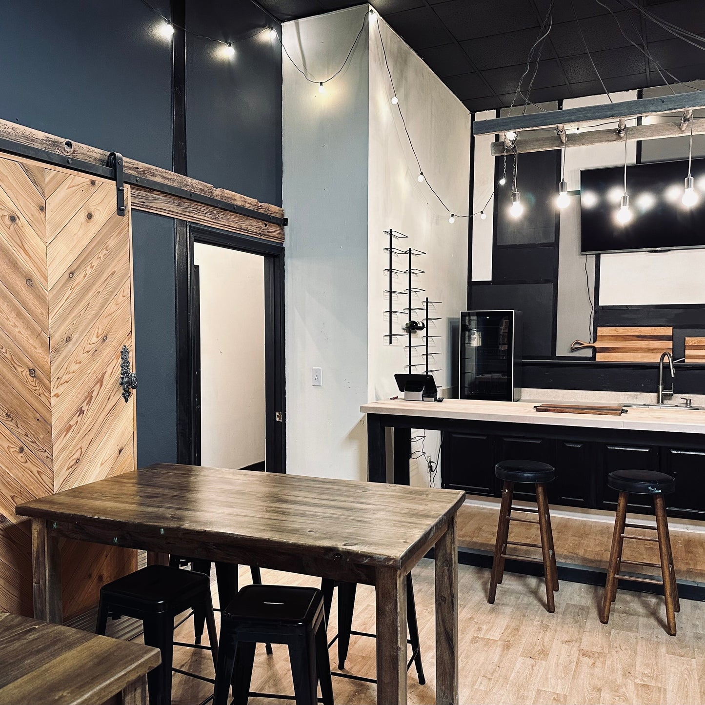 Modern kitchen with wooden table and stools, black appliances, and a wooden sliding door.