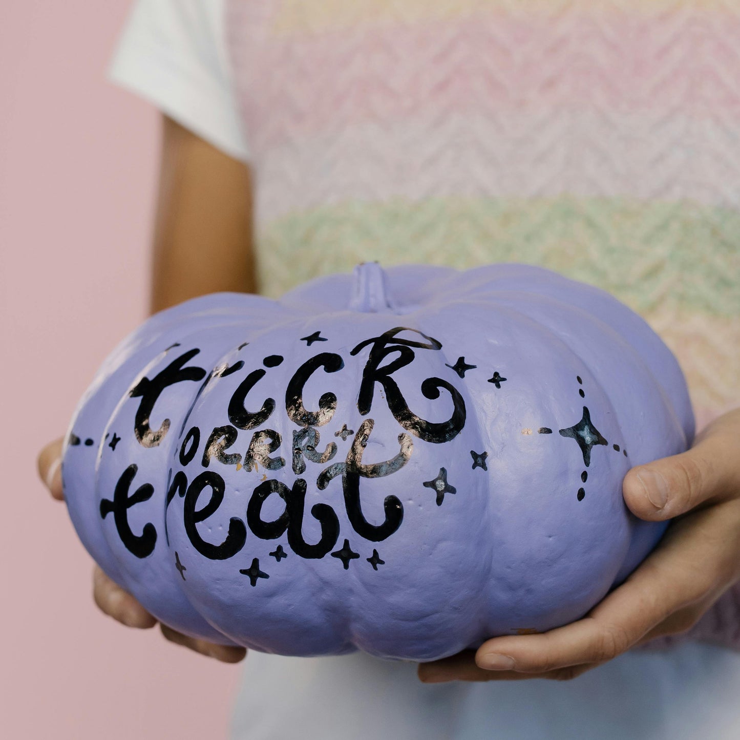 Person holding a purple pumpkin with 'trick or treat' text against a pink background