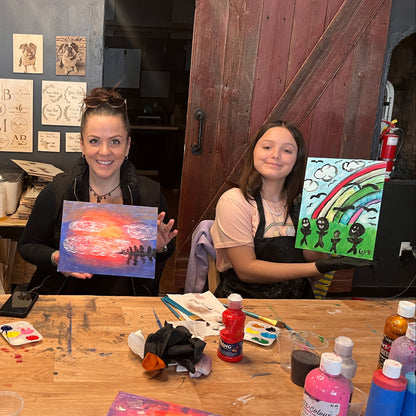 Three people sitting at a table with art supplies and artworks.