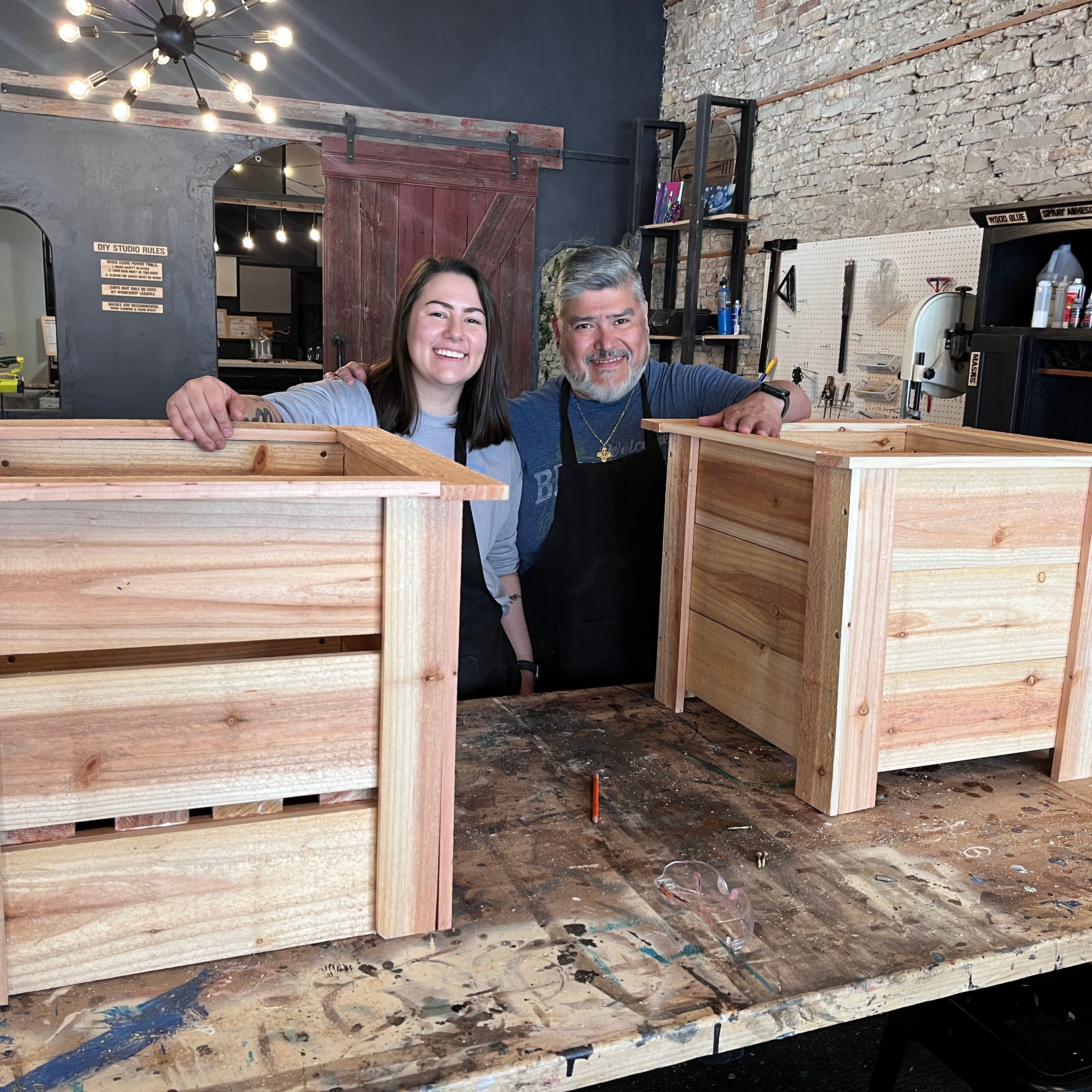 Two people standing by wooden planter boxes in a workshop setting.