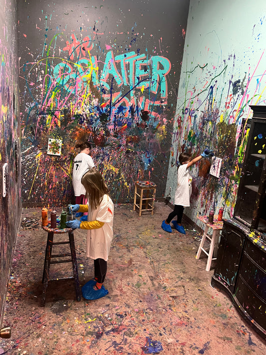 Four children in a splatter room with colorful painted art on the walls and floor.