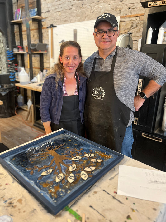 Two people in a workshop with a decorative wooden laser-cut family tree framed art piece with an epoxy background on a table