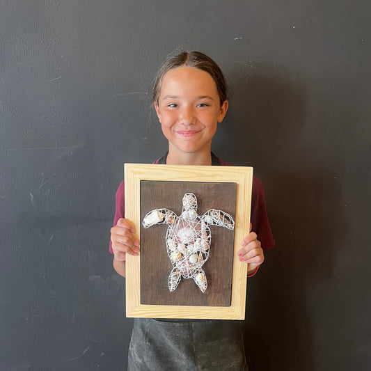 Girl holding framed string art of a turtle with shells against a black background