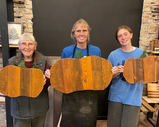 Three women holding wooden cutouts of pumpkins against a stone wall background.