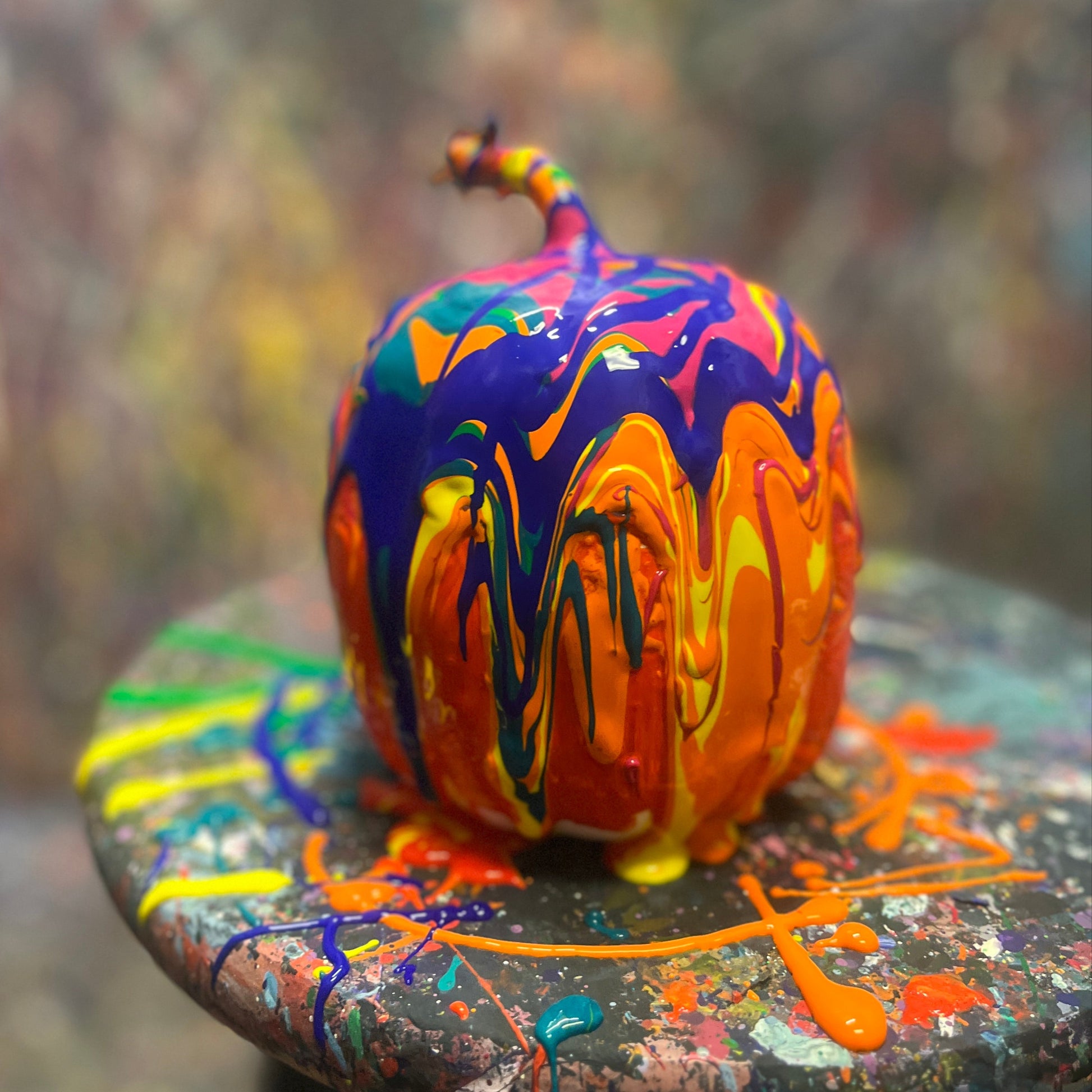 Colorfully splatter painted pumpkin on a stool with a blurred background