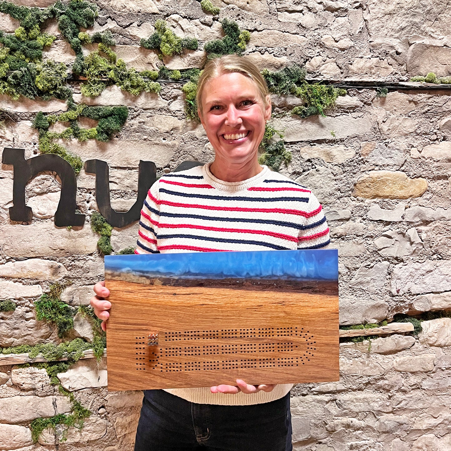 Woman holding an Epoxy River Cribbage Board by a stone wall
