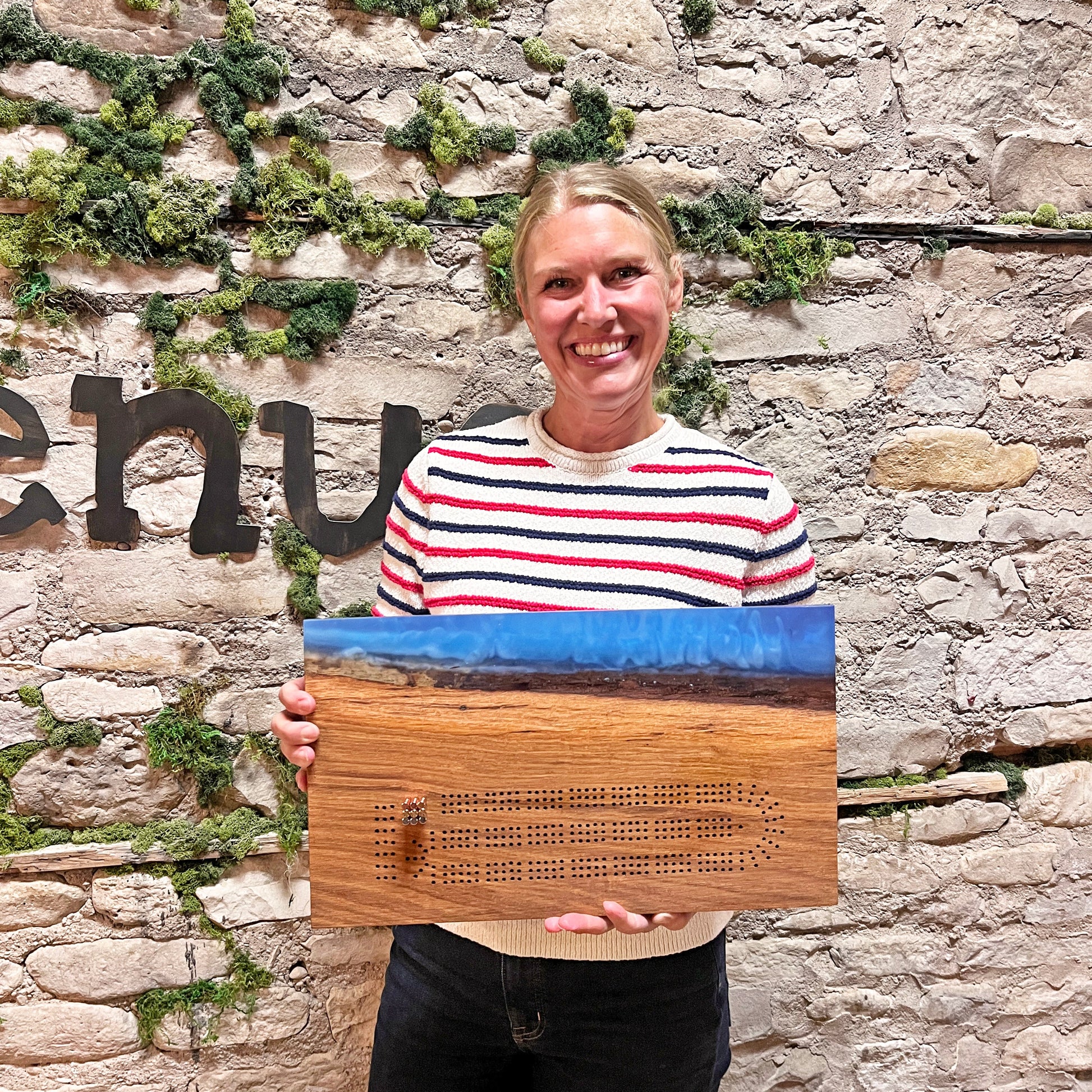 Person holding a wooden board with engraved text against a stone wall.
