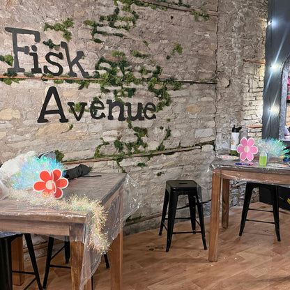 Dining area with wooden tables and chairs against a stone wall with 'Fisk Avenue' branding.