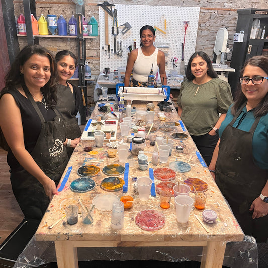 Group of people making epoxy coasters around a table with art supplies in a workshop setting.