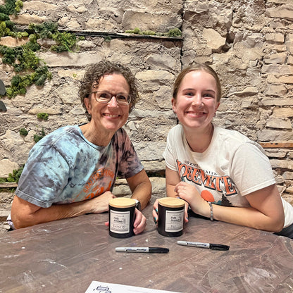 Two people sitting at a table with candles and markers against a stone wall.