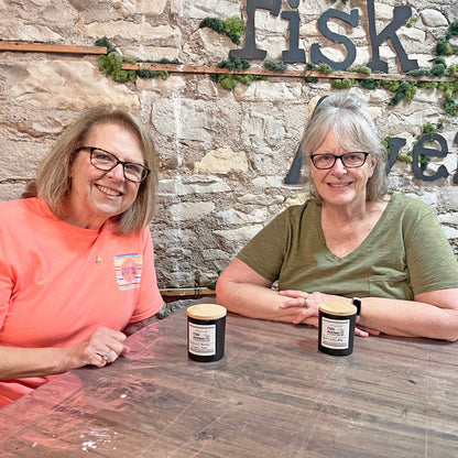 Two women sitting at a table with candles in front of a stone wall with 'Fisk Avenue' sign.