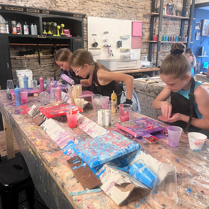 Girls adding crystals to fluid art paintings at a workshop table in stone studio setting.