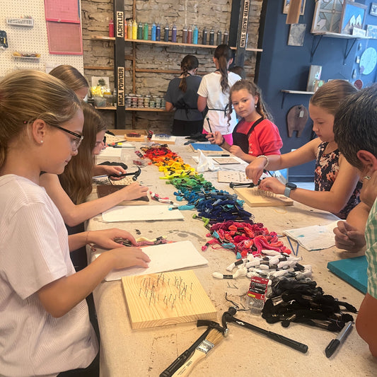 Children engaged in a string art craft activity at a table with various materials.