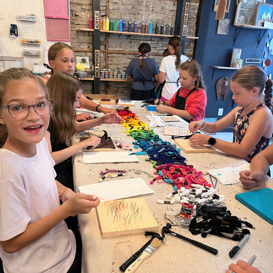 Children working on a string art craft project at a table with various materials
