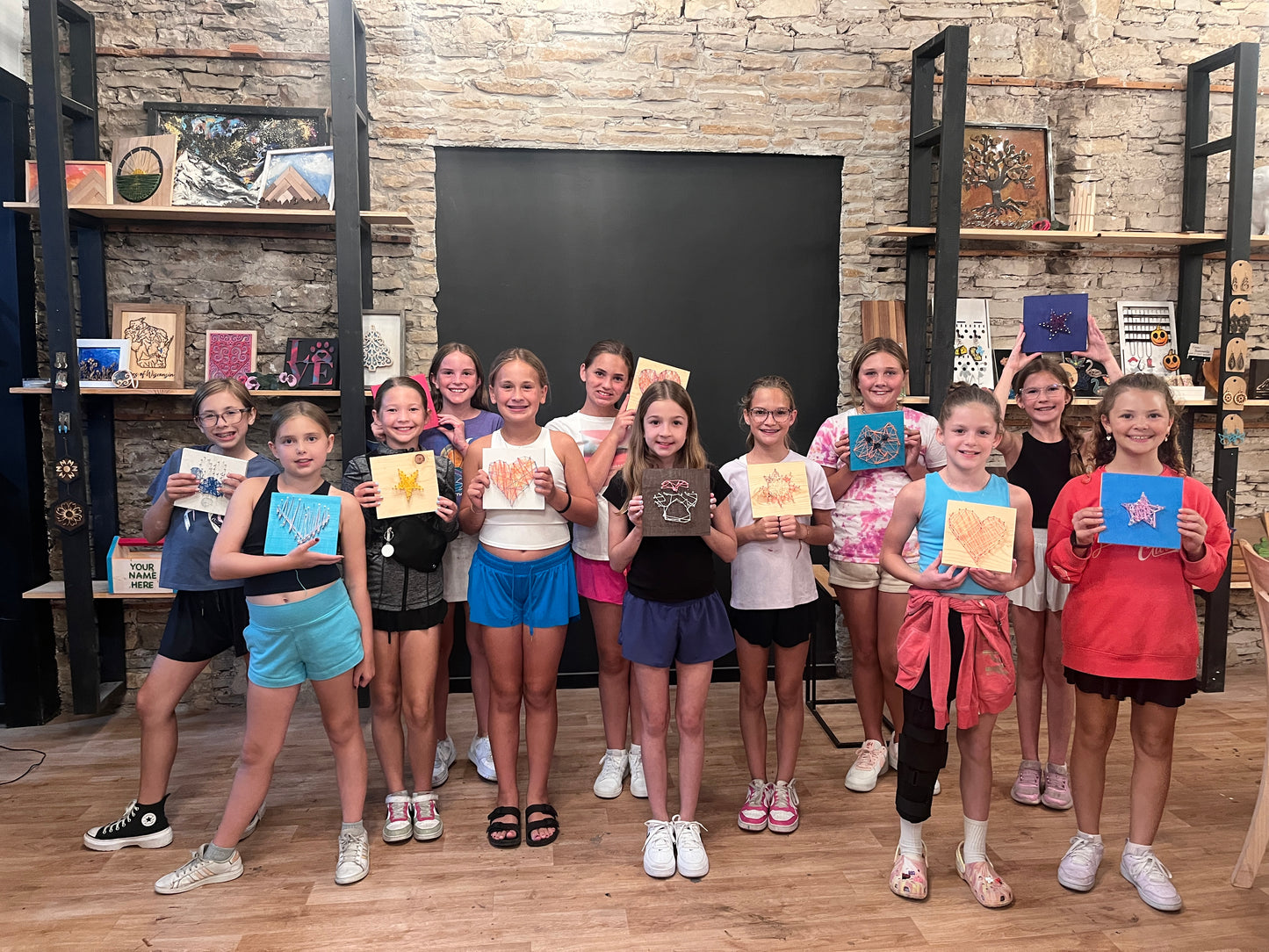 Group of children holding up their artwork in a room with shelves and a blackboard.