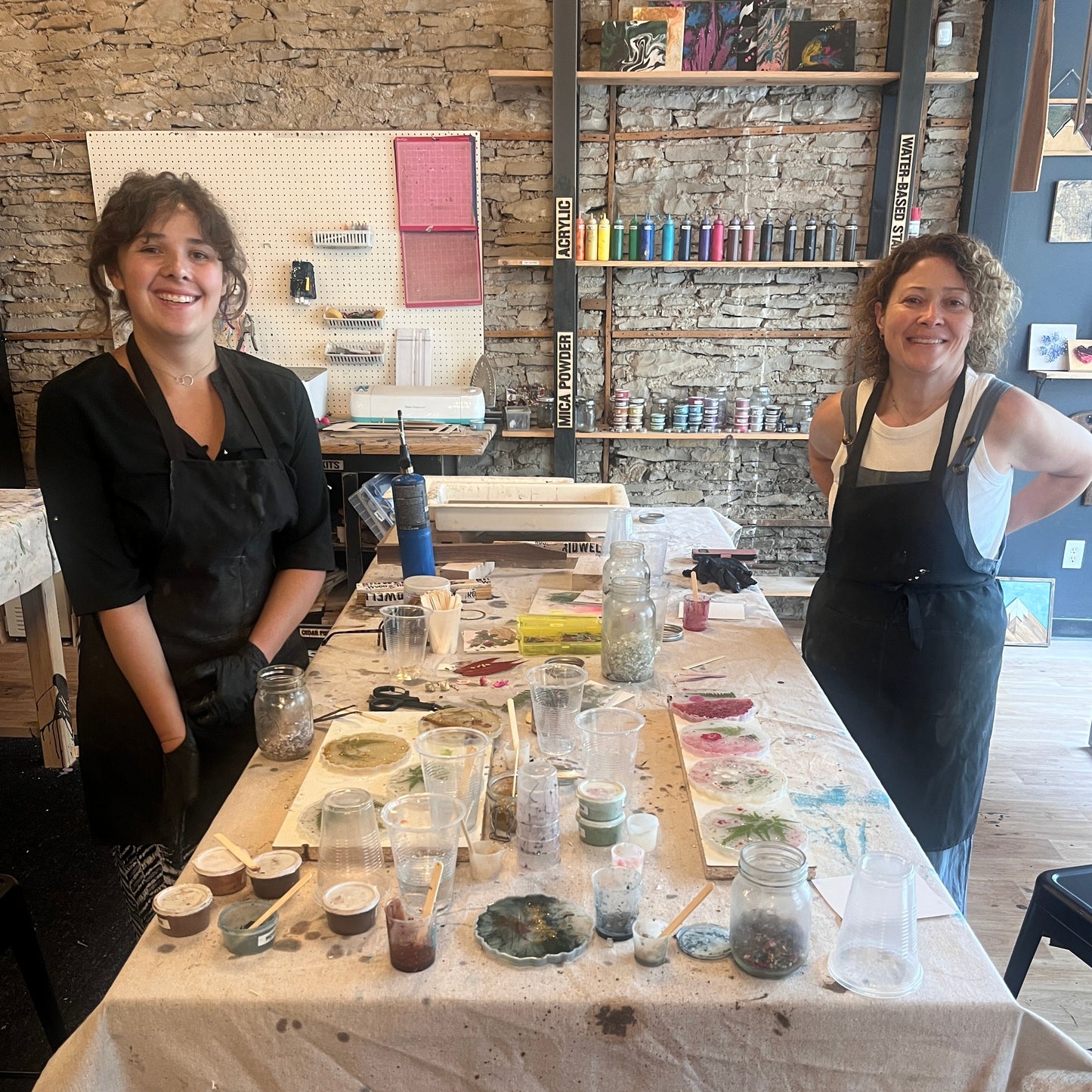 People standing in front of a table with epoxy floral coaster supplies in a workshop setting.