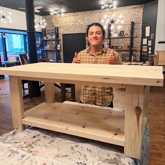Person standing behind a wooden coffee table in a studio with shelves and decor.