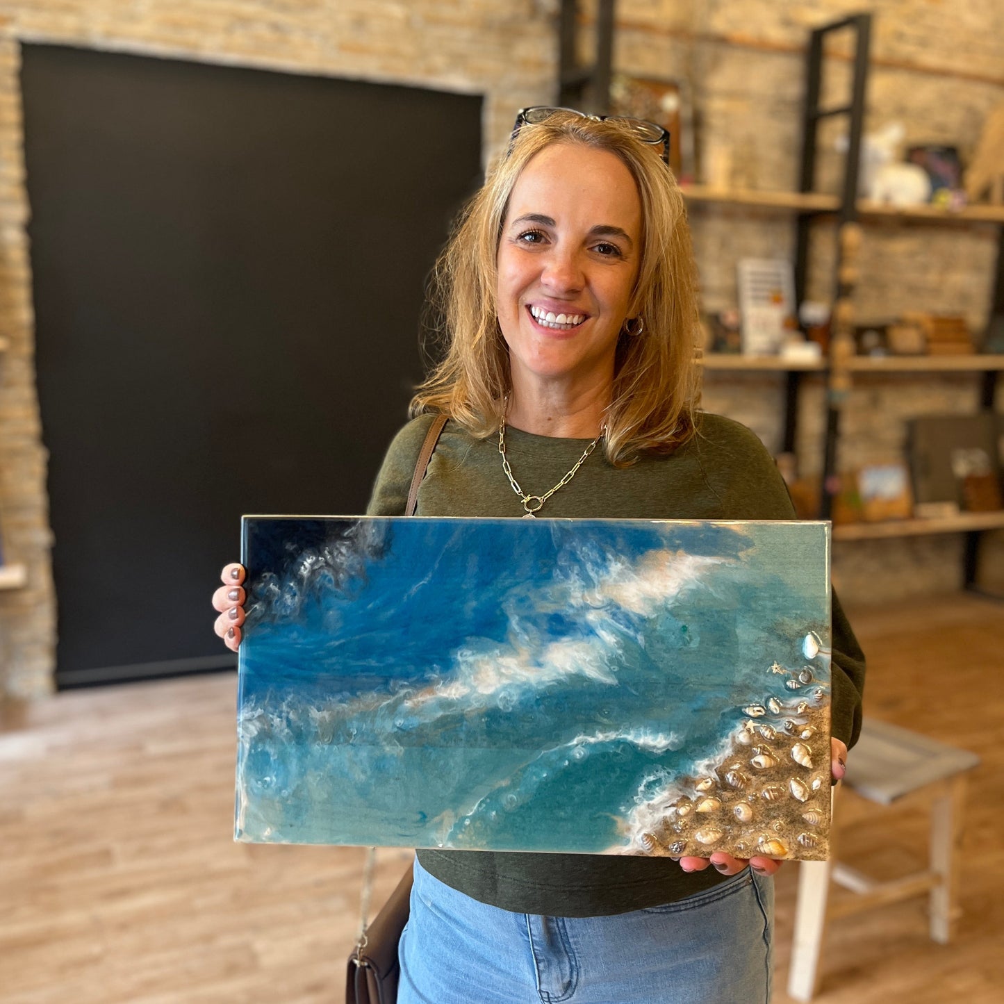 Woman holding a blue epoxy ocean pour tray in a room with wooden shelves.