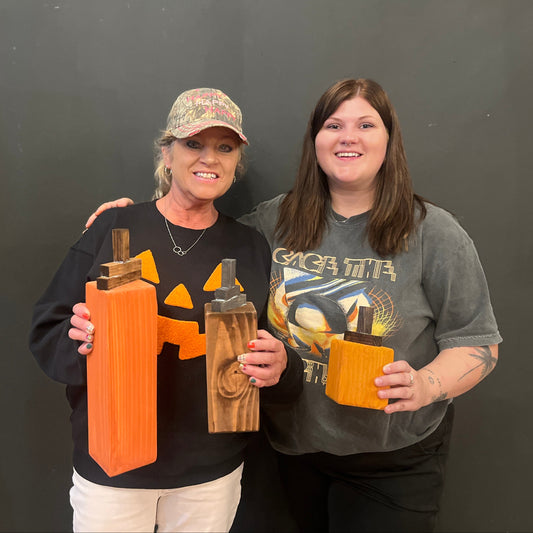 Two women holding wooden pumpkin crafts against a black background