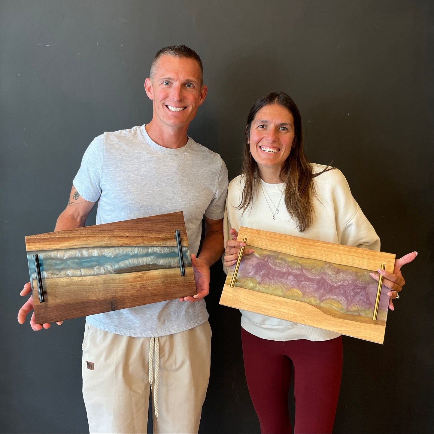 Two people holding wooden Epoxy River Trays against a dark studio wall.
