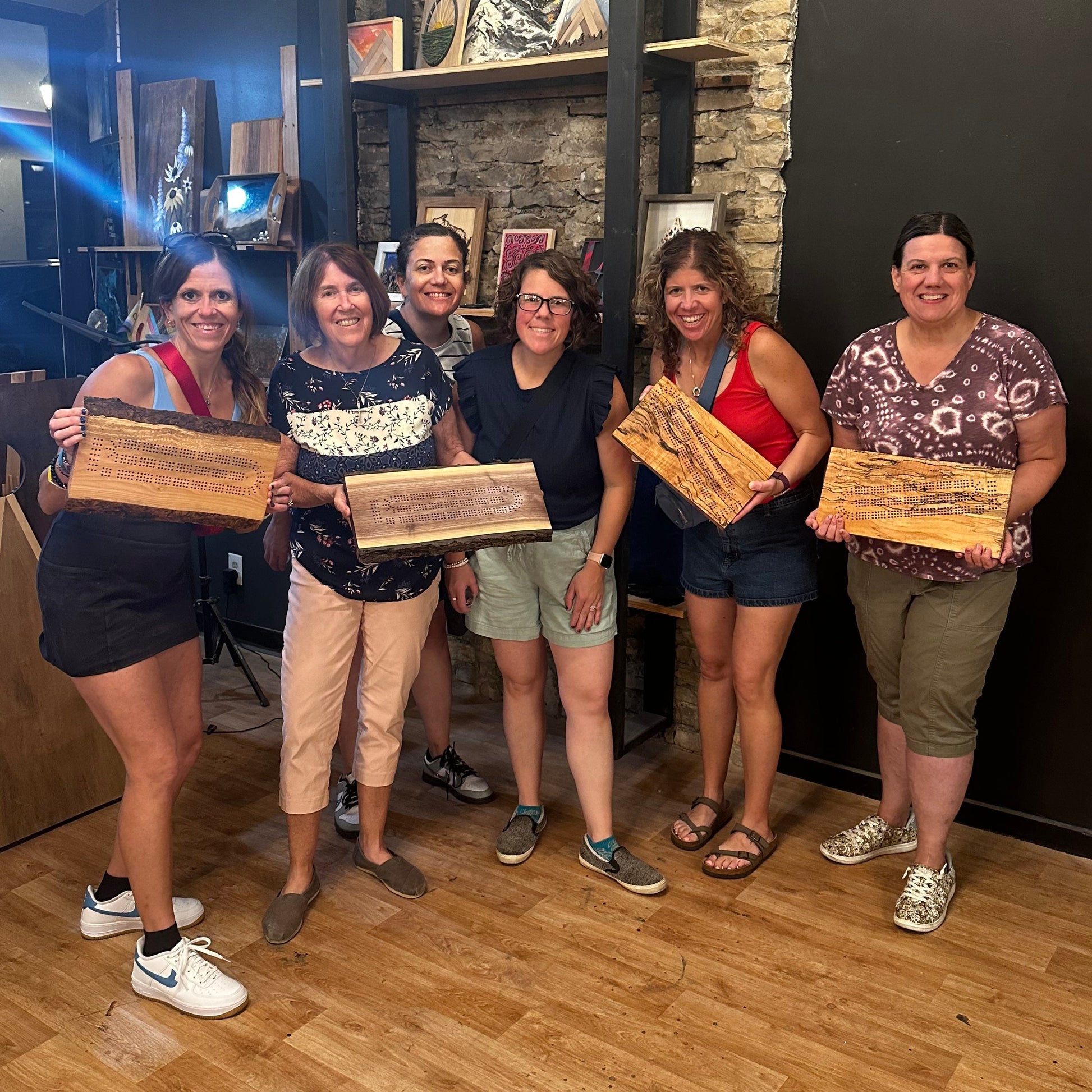 Group of five women holding wooden ciribbage boards in a studio with stone walls and wooden floors.