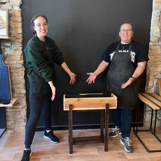 Two people standing by a wooden planter in a studio with wooden floors and stone walls.