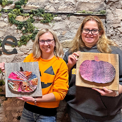 Two people holding copper pumpkin art in front of a stone wall with 'Fisk Avenue' sign.