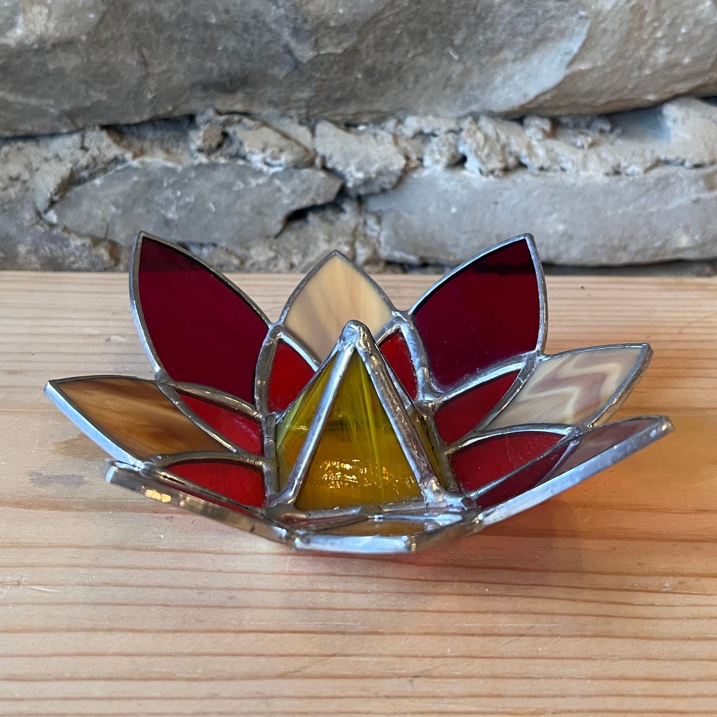 Stained glass lotus flower on a wooden surface with a stone wall background