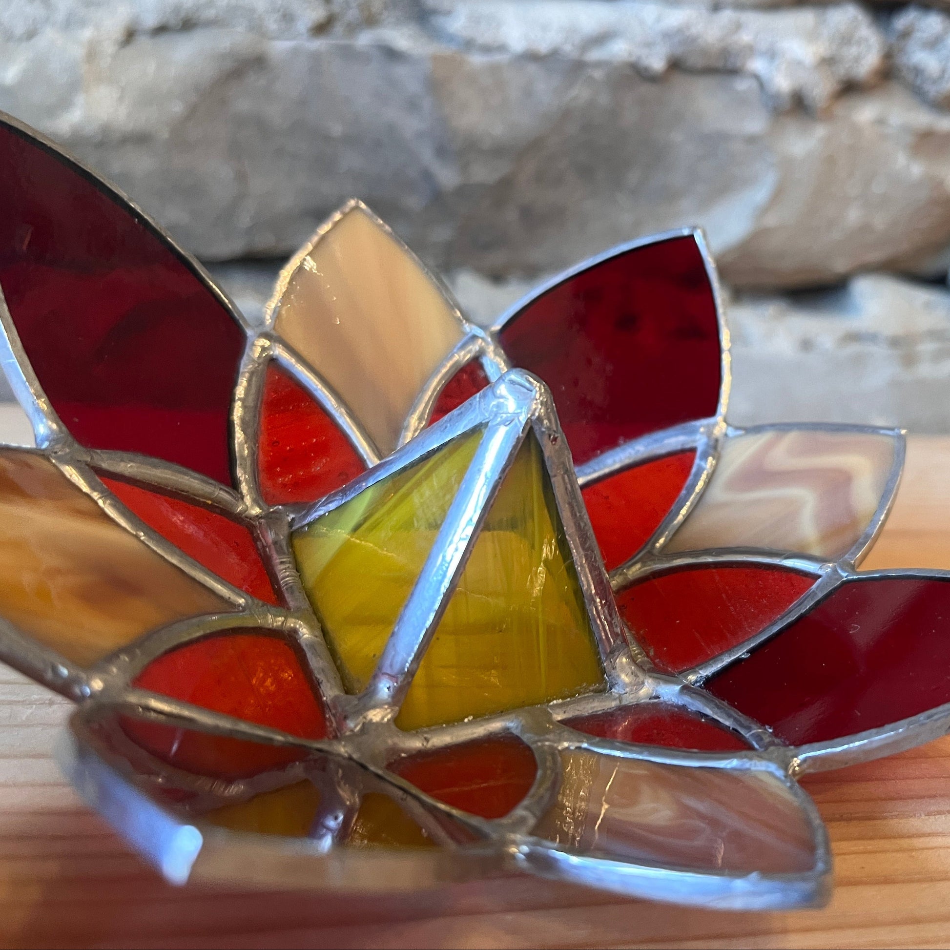 Stained glass flower on a wooden surface with a stone wall background