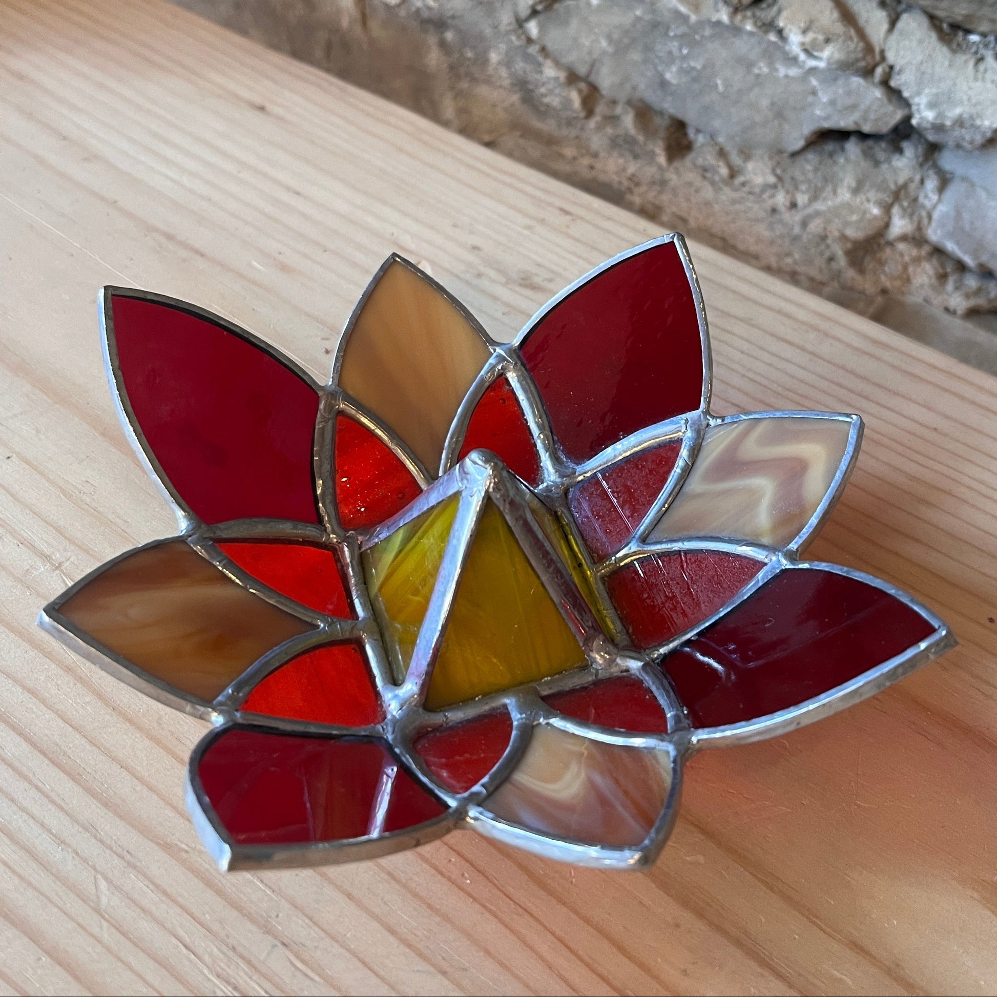 Stained glass lotus flower on a wooden surface with a stone wall background