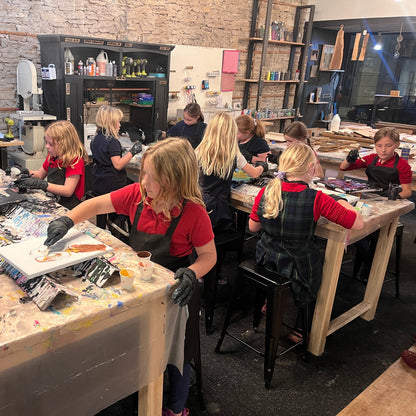 Children working on art projects in a workshop setting with tables and supplies.