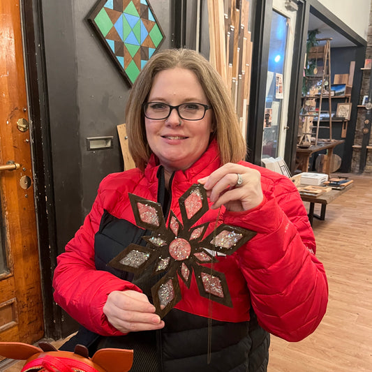 Person wearing a red jacket with a epoxy snowflake suncatcher, standing in front of a studio setting.