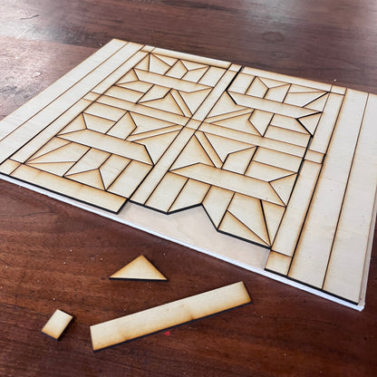 A wooden geometric design with laser-cut leaf patterned pieces, displayed on a dark wood tabletop with a few loose pieces in front.