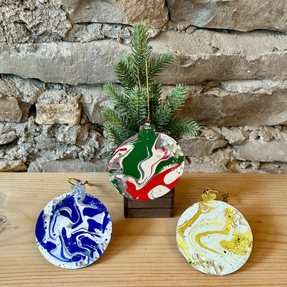 Three fluid art Christmas ornaments on a wooden surface and mini tree with a stone wall background.