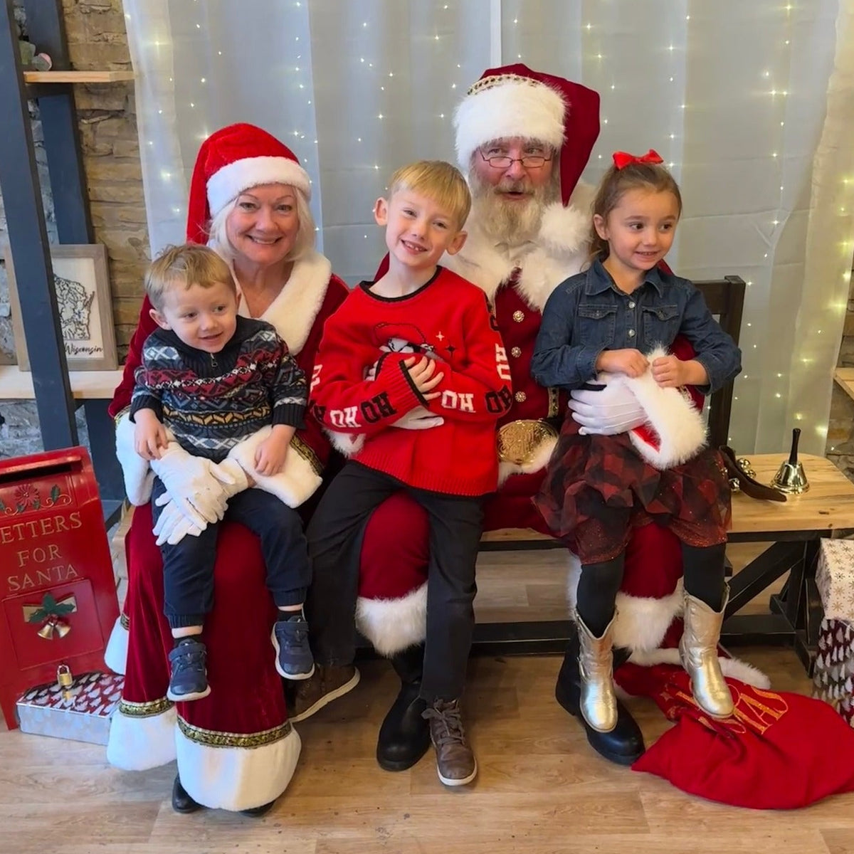 Three children posing with Santa Claus and Mrs. Claus in a festive indoor setting.