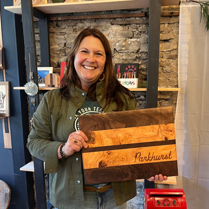 Woman holding a wooden cutting board with a 'Parkhurst' family name engraving in a store setting.