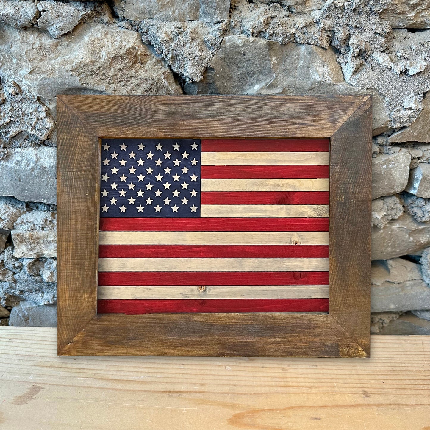 Wooden-framed American flag against a stone wall background