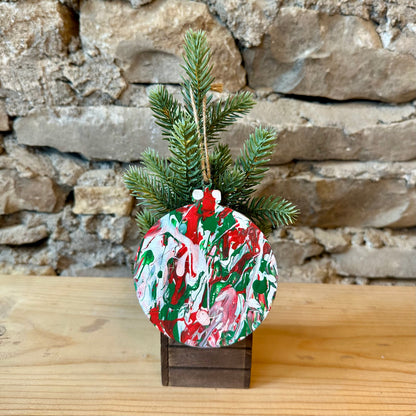 Decorative wooden Christmas ornament with a splatter painted design on a mini tree against a stone wall.